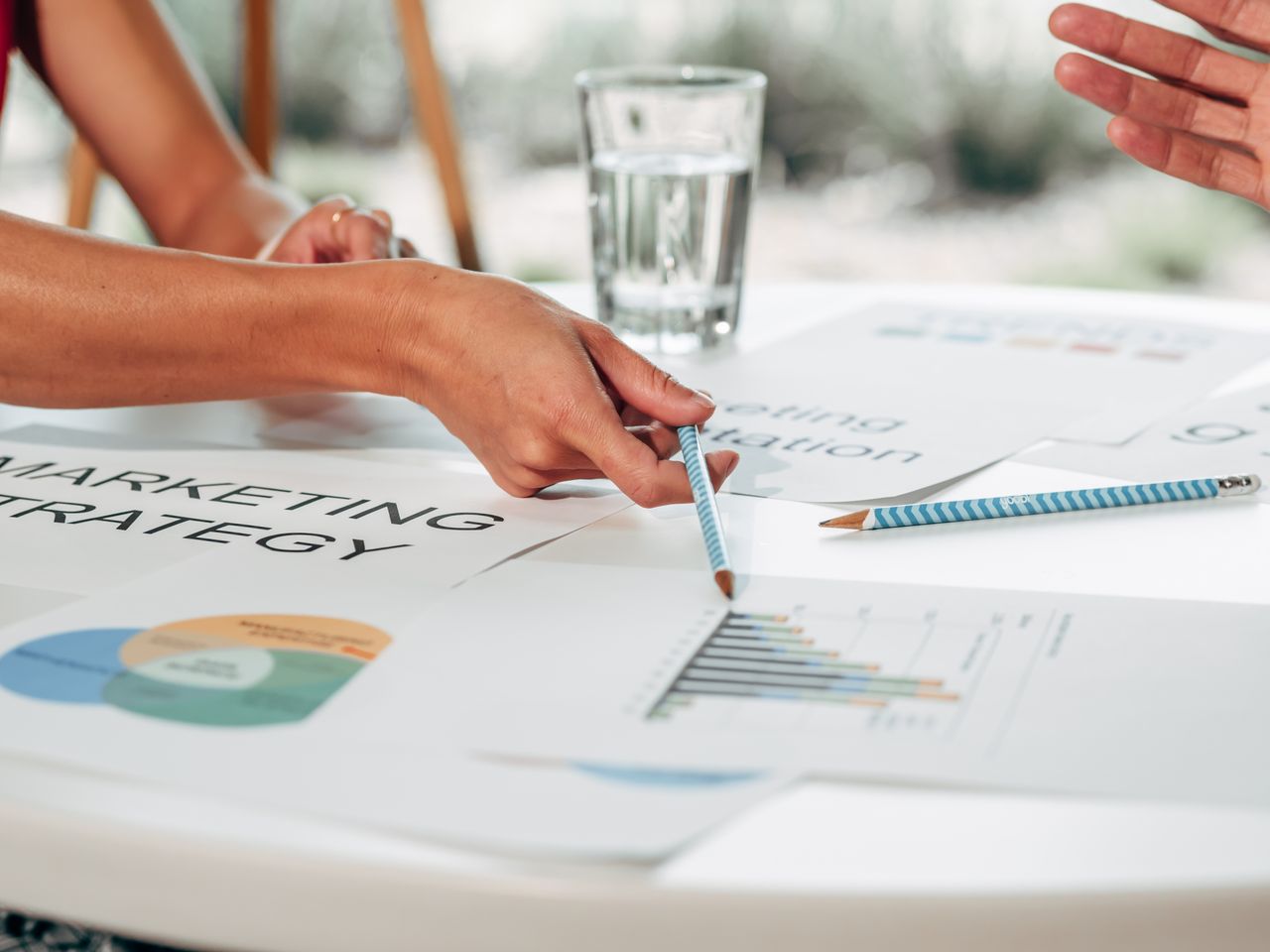 Des mains discutant d’une stratégie marketing avec des graphiques dans un cadre de bureau.
